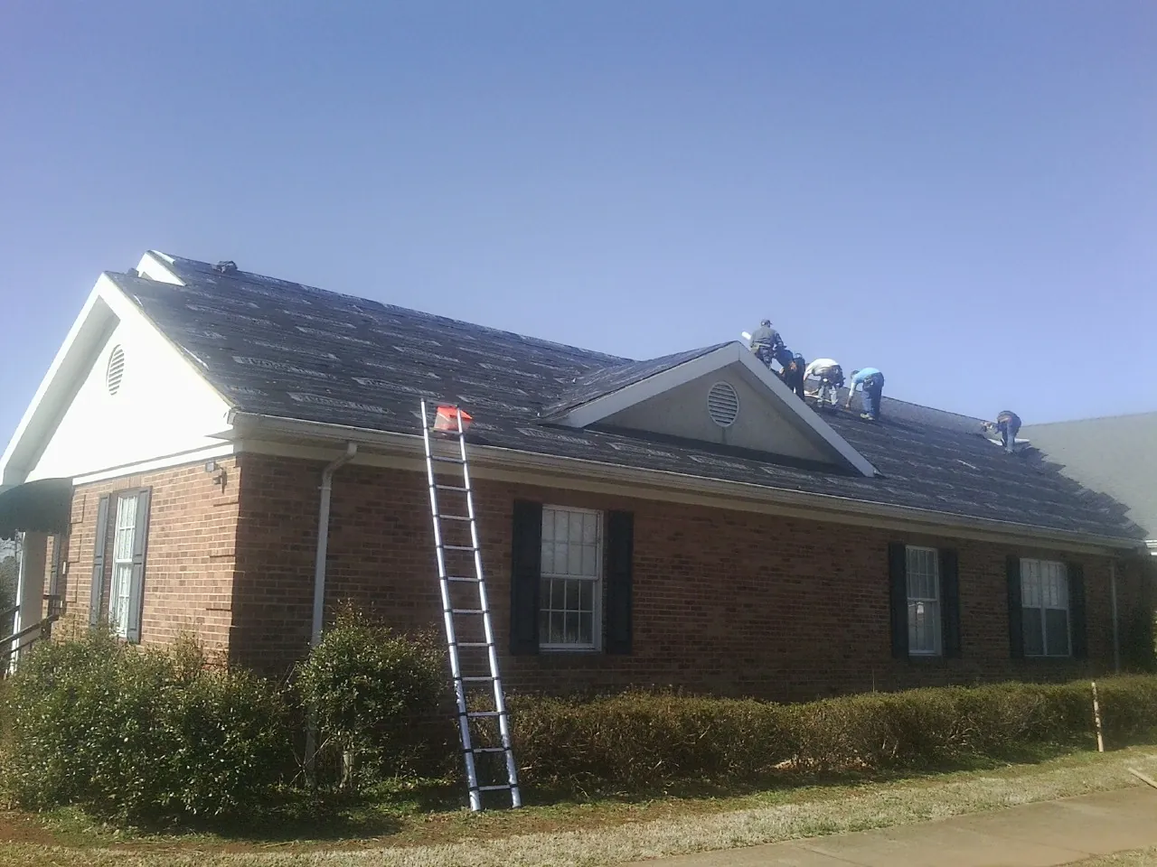 Crew tearing shingles off a brick ranch roof with a ladder set — Emergency Roof Repair work by our crew in Orchard