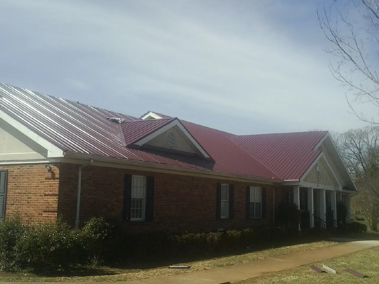 Red metal roof with gabled entries on a long brick building, from a Hail Damage Roof Repair job in Orchard