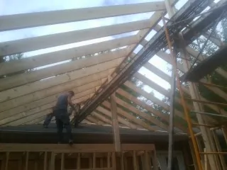 Rafters going up over a new addition with a worker on the wall in Orchard