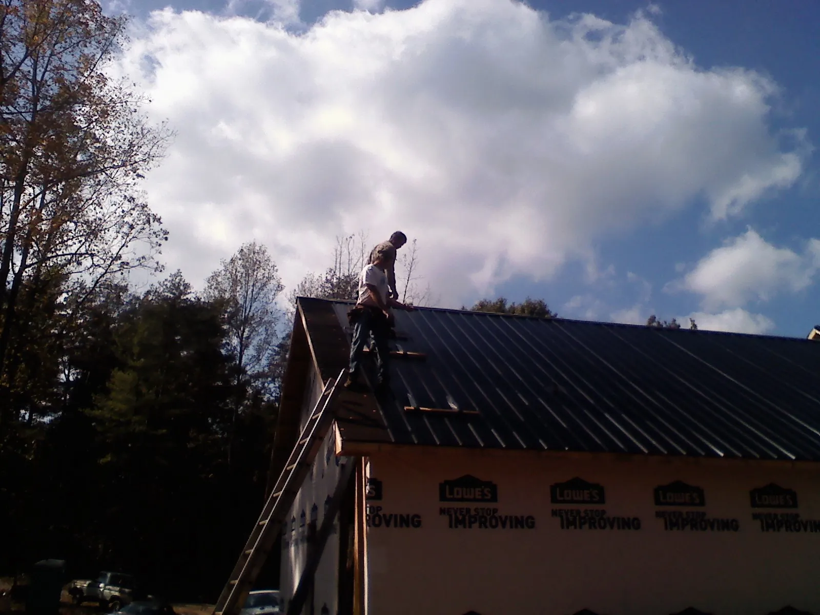 Roofer fastening dark metal panels high against a cloudy sky, from a Roof Inspection job in Orchard