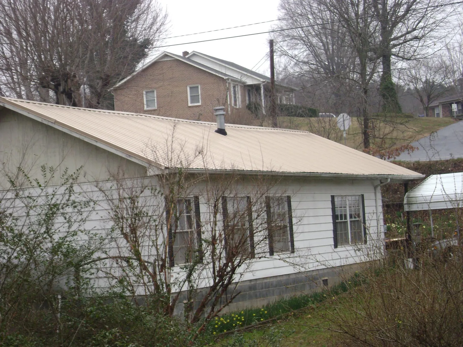 Tan metal roof on a white sided house set into a hillside — Commercial Roofing by Roofing Brothers in Orchard
